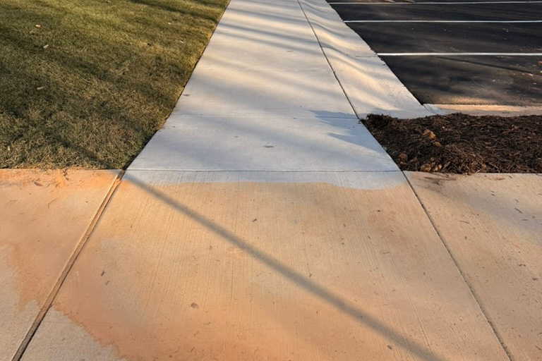 Concrete sidewalk with a cleaned section next to a section stained orange